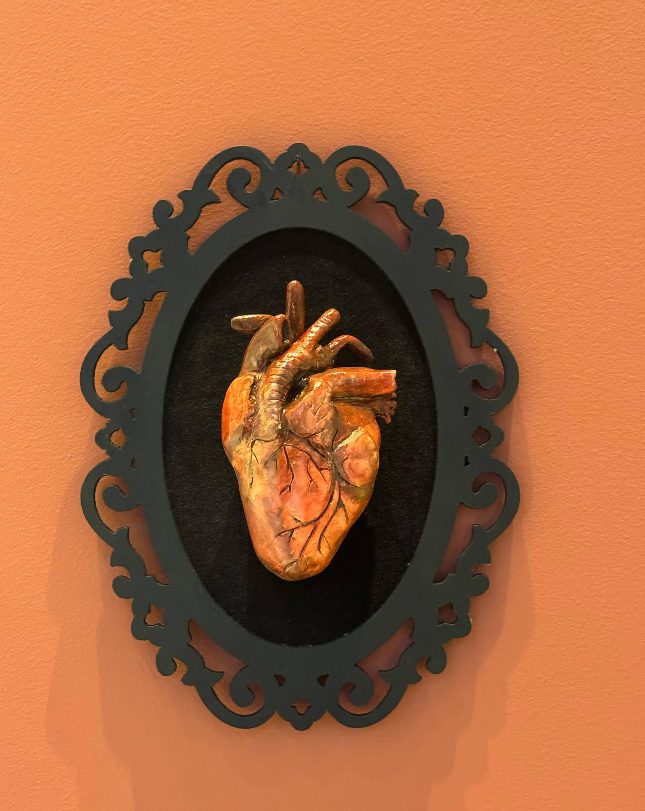 Coração anatômico em relevo, dentro de uma moldura preta ornamentada, na parede do studio.
