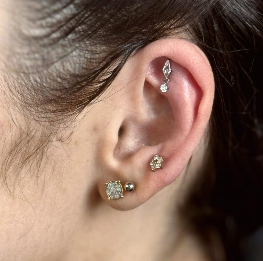 Orelha com quatro piercings: uma joia pendente na parte de cima e três brincos no lóbulo.