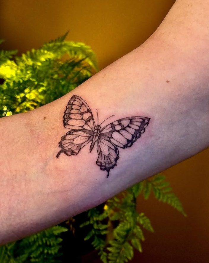 Tattoo de borboleta em preto e cinza no braço.