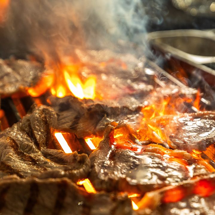 Carnes na grelha, com as chamas da brasa subindo entre os cortes.