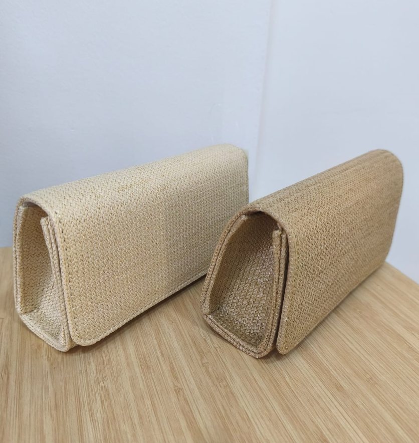 Três bolsas de mão em palha, em tons de bege, empilhadas.