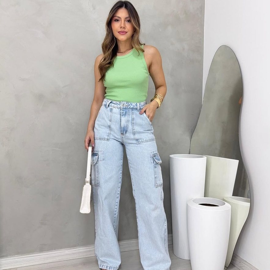 Mulher com regata verde-clara, calça jeans clara e bolsa branca pequena.
