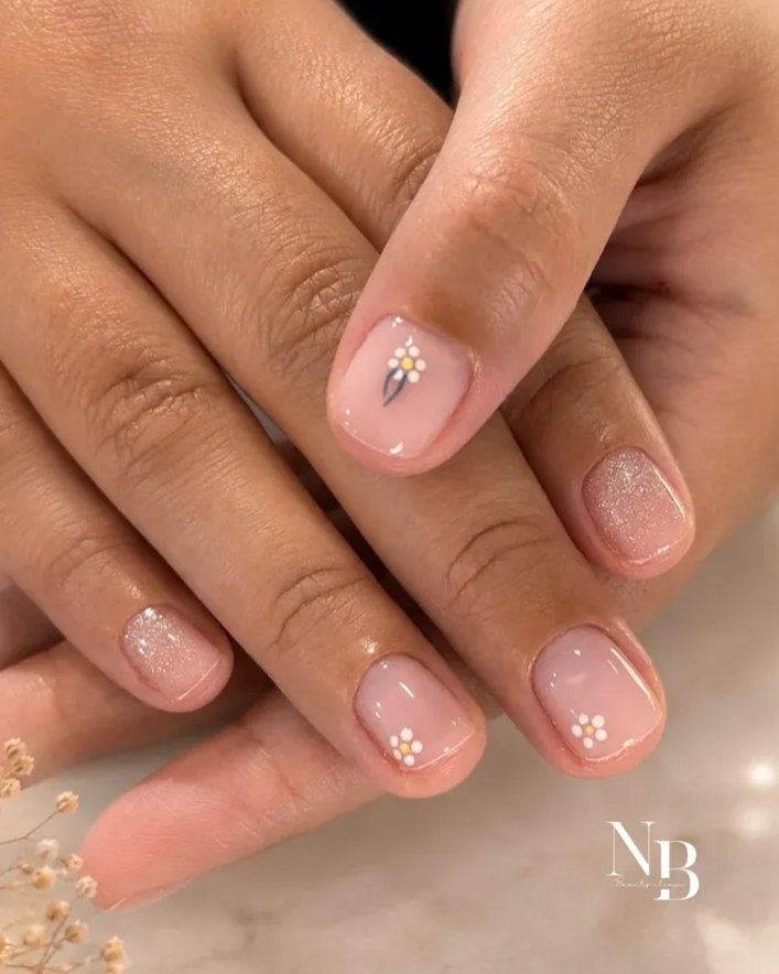 Mãos com unhas nude e pequenas flores brancas desenhadas.