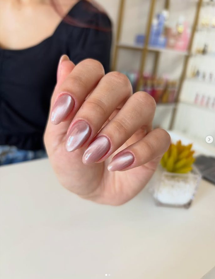Mão com unhas em gel nude amendoadas, apoiada na bancada da clínica.