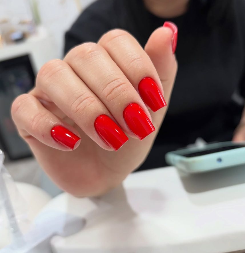Mão com unhas quadradas em vermelho vivo, sobre a bancada.