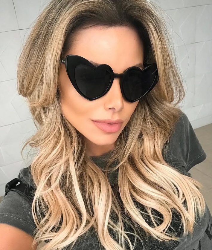 Mulher loira usando óculos de sol pretos com lentes em formato de coração.