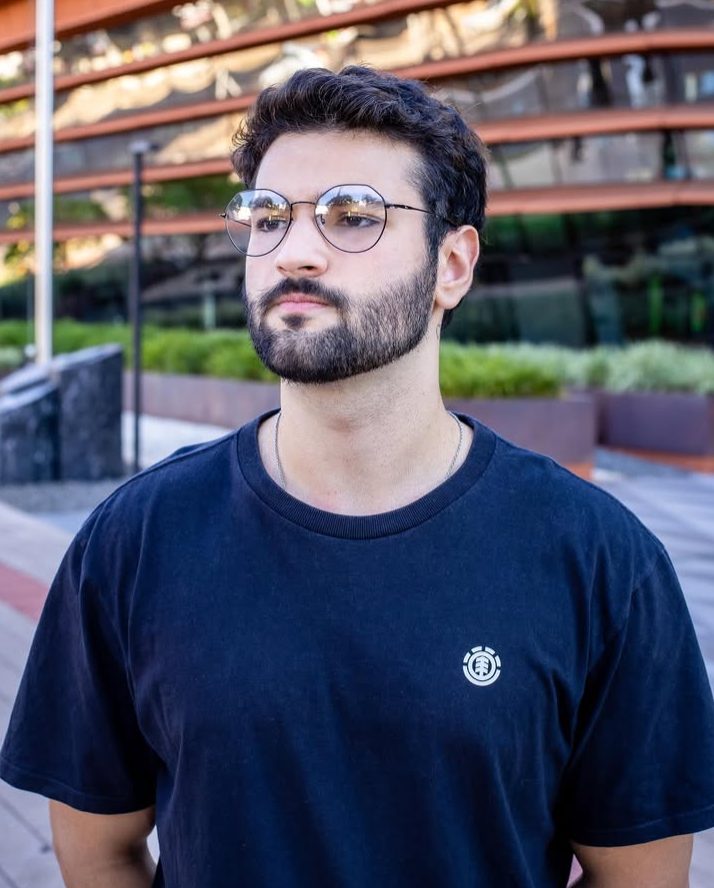 Homem de barba usando óculos de grau redondos, com armação fina de metal.