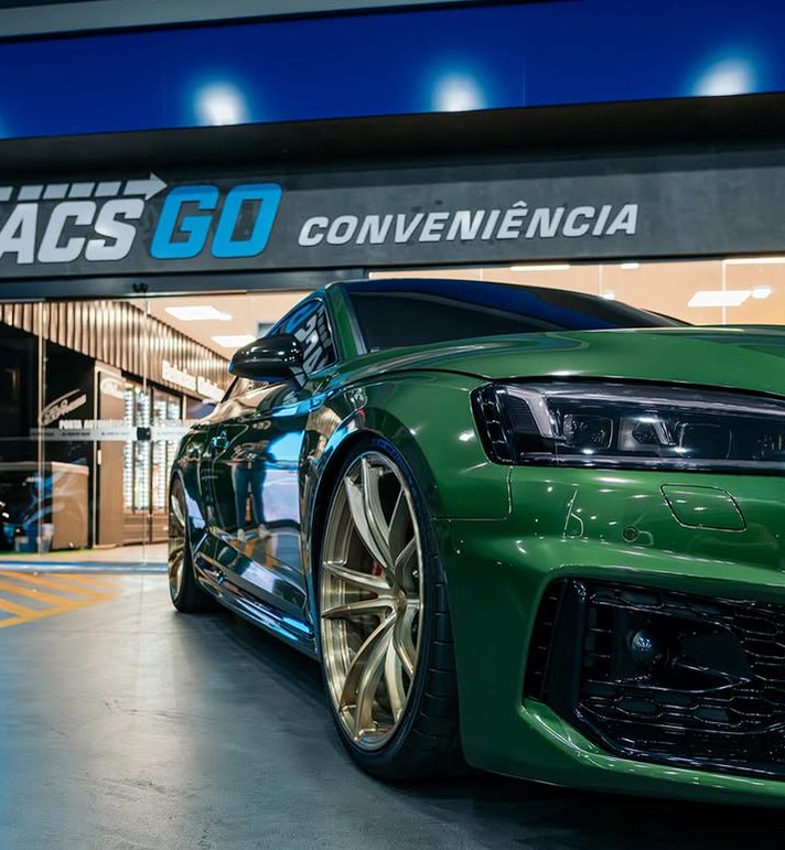 Fachada da conveniência Tacs Go, com um carro verde estacionado em frente.