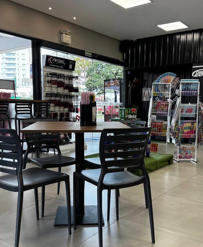 Interior da conveniência, com mesas altas, expositores e a porta aberta para a pista.