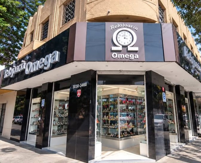 Fachada da Relojoaria Omega, em uma esquina da Avenida Brasil: letreiro preto com o logo e vitrines iluminadas.