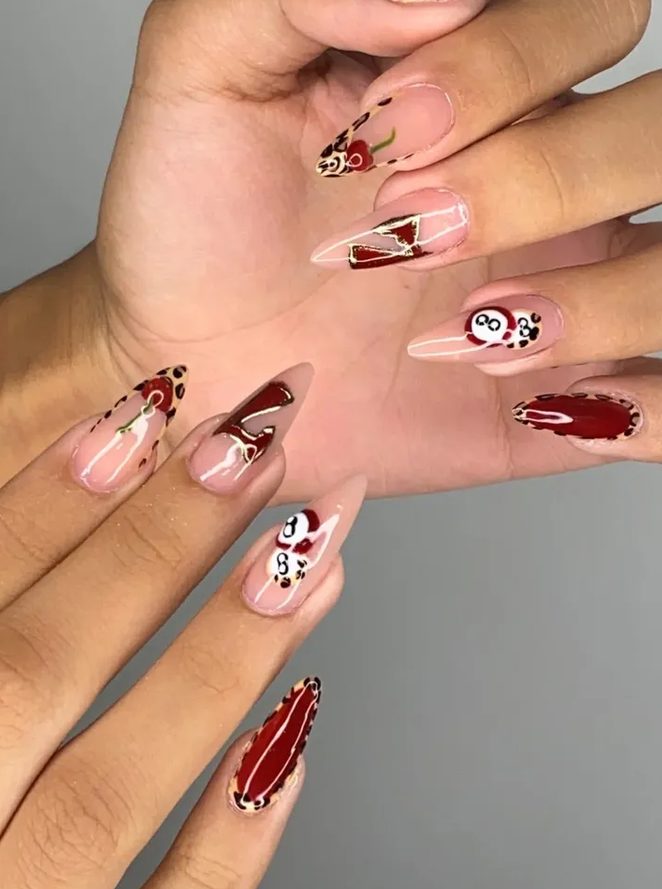 Mãos com unhas alongadas e nail art em vermelho: cerejas, bola oito e detalhes de oncinha.