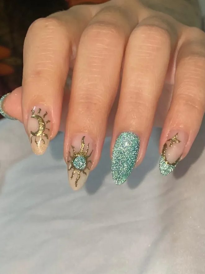 Unhas com nail art de sol e lua em dourado e uma unha inteira em glitter verde.